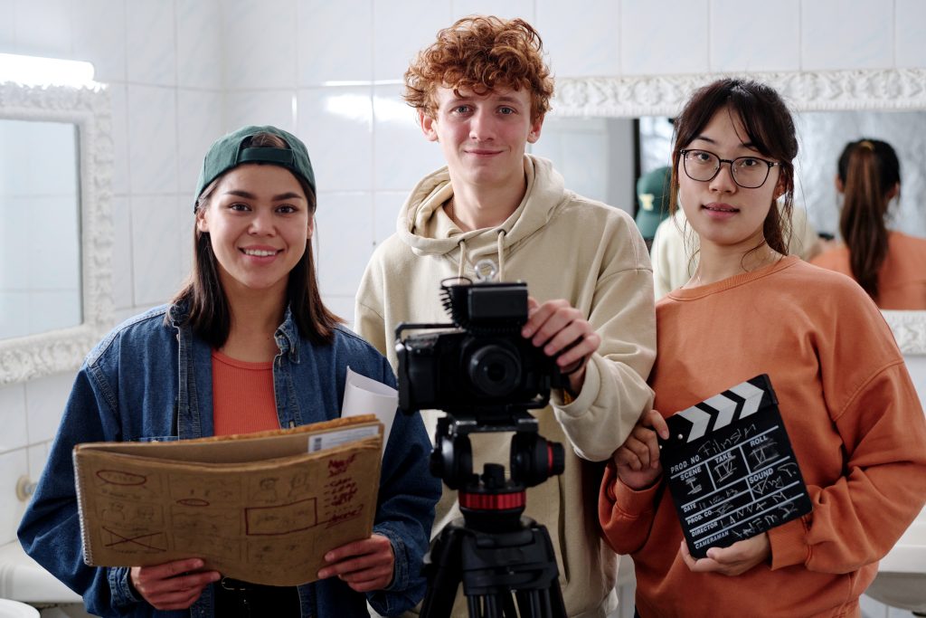 3 young student filmmakers in a public area holding film equipment